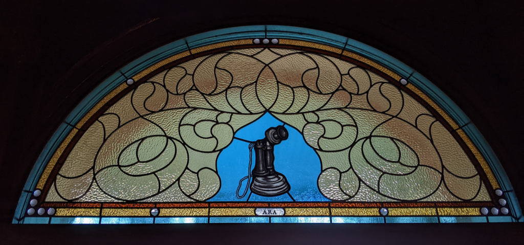 A stained glass window that includes the image of an old-time telephone in the design