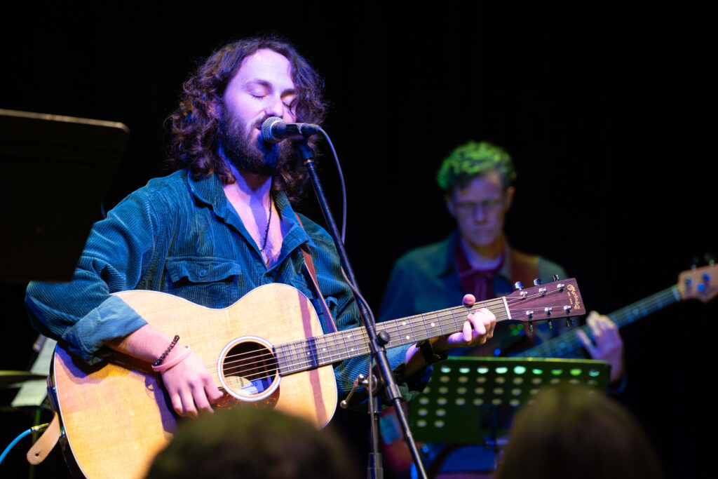 Witness trips performed a song accompanied by his acoustic guitar. A member of Collective Unconscious is seen in the background