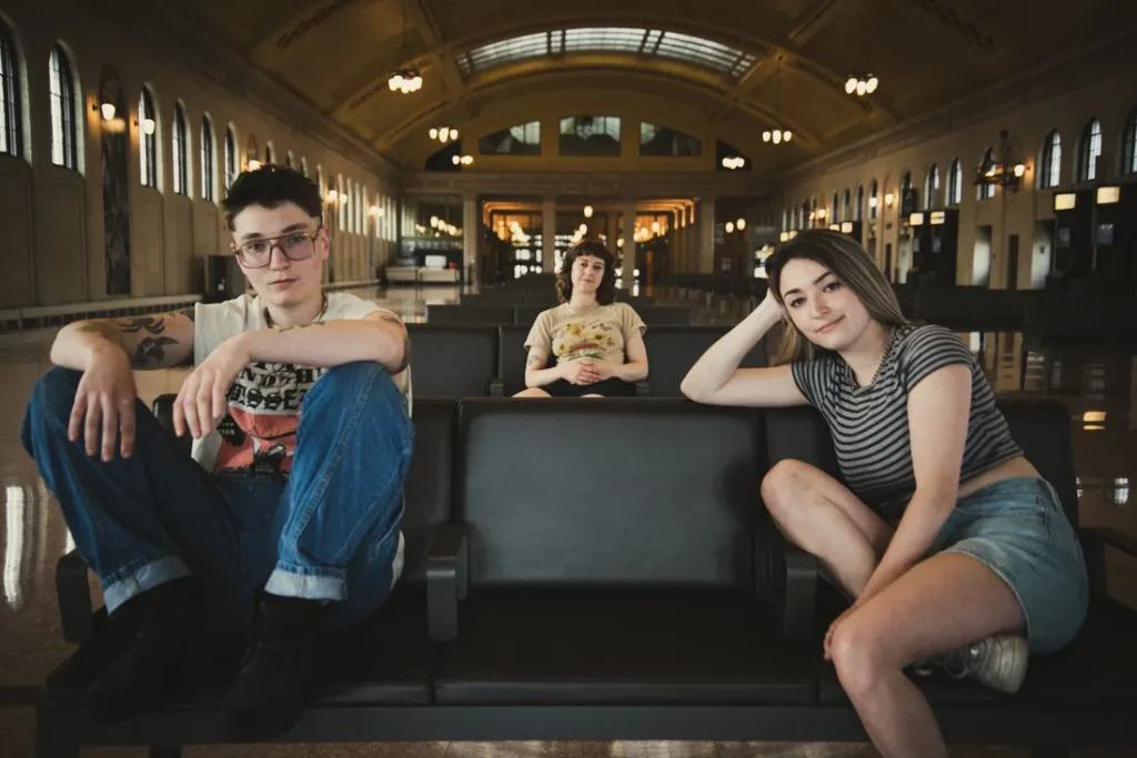 The members of the band Mary Jam sit on benches in a train station