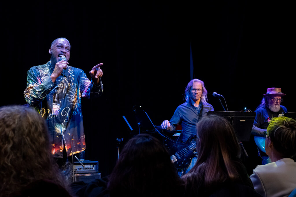 Jaybee sings to the audience, backed by Jeff Engholm and Muggsy Lauer of Collective Unconscious