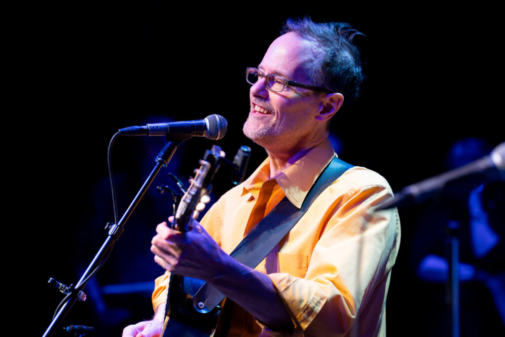 Matt Wilson plays his guitar and sings into a microphone