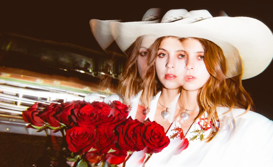 A photo of Mikaela Davis. She wears a white cowboy hat and holds a bouquet of roses. The image is