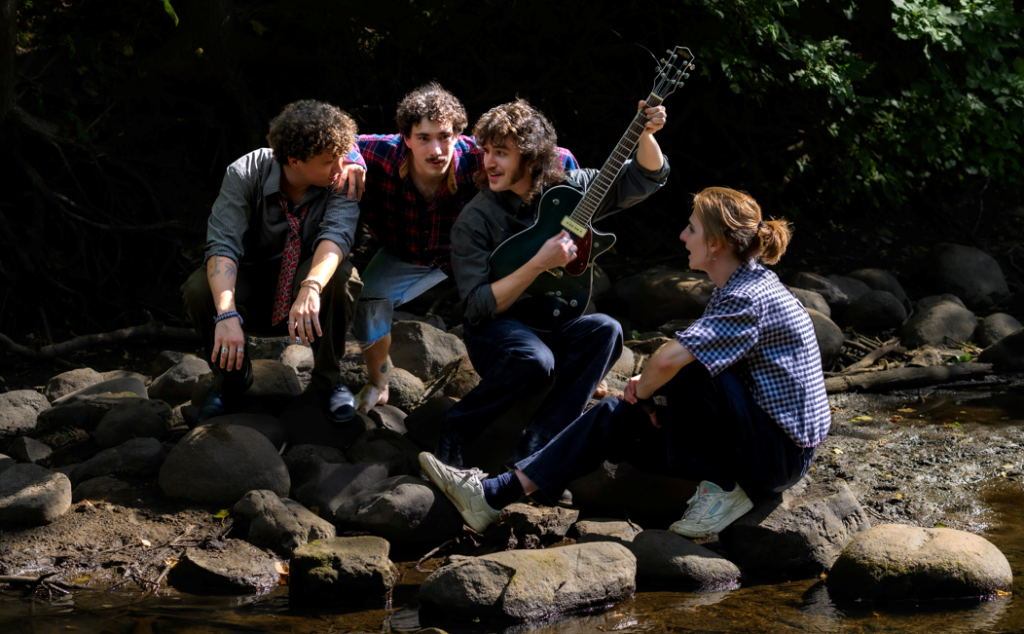 The four members of the band Stonewalker performing while sitting on rocks by the edge of a body of water